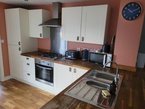 a kitchen with white cabinets and a sink and a clock at Little Willows in Handcross