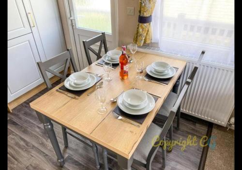 a wooden table with plates and wine glasses on it at MP413 - Camber Sands Holiday Park - Close to Facilities - Free Wifi - Sleeps 8 - Large Decking in Camber