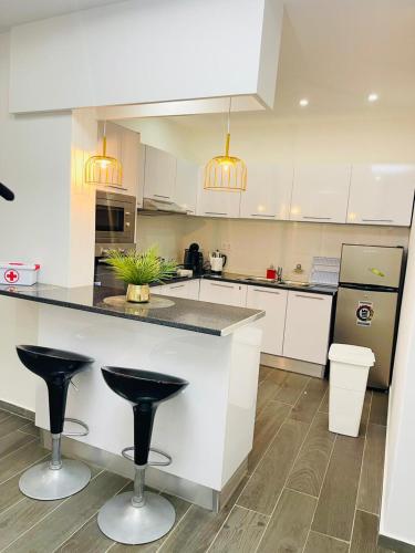 a kitchen with white cabinets and black counter stools at Résidence Cazino Apartamentos in Praia