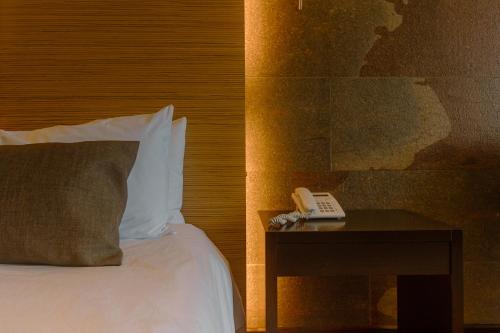 a bed with a pillow and a phone on a table at Rayentray Grand Hotel in Puerto Madryn