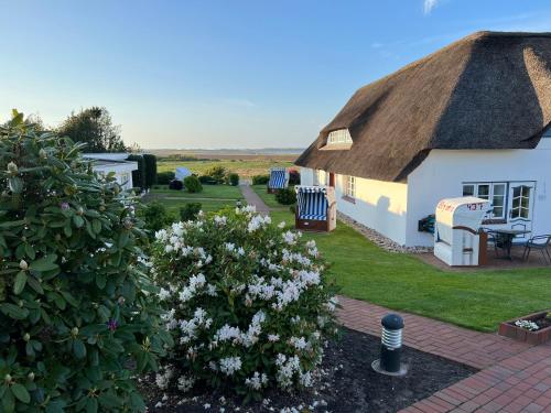 a white cottage with a thatched roof and a garden at Haus Amanda in Norddorf