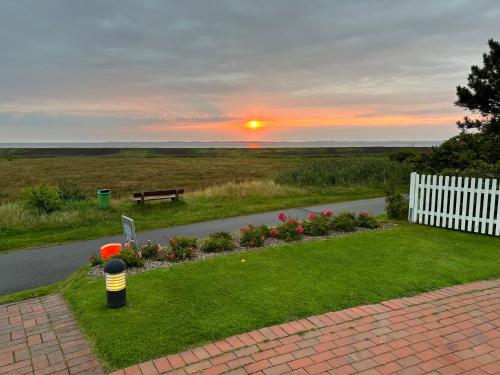 a sunset over a garden with a bench and flowers at Haus Amanda in Norddorf