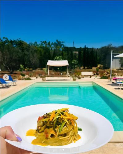 a person holding a plate of pasta in front of a pool at B&B DOÑA FLOR in Parabita