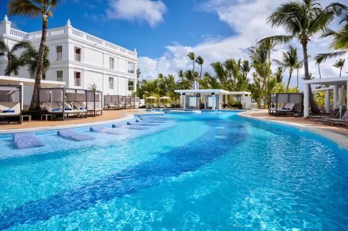 a large pool with palm trees and a white building at Riu Palace Bavaro - All Inclusive in Punta Cana