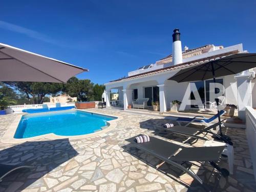 a villa with a swimming pool and two chairs and an umbrella at Peaceful villa with sea view close to Carvoeiro in Carvoeiro