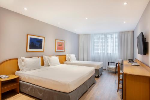 a hotel room with two beds and a desk at Windsor Guanabara Hotel in Rio de Janeiro