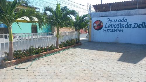 a building with a fence and palm trees and a sign at Pousada Lençóis do Delta in Tutóia