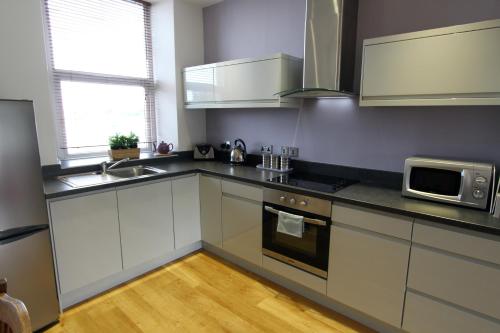 a kitchen with white cabinets and a sink and a microwave at Wynnstay Apartment, Harbour and Mountain Views in Barmouth