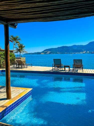 a swimming pool with two chairs and the water at Pousada Vila das Velas in Ilhabela