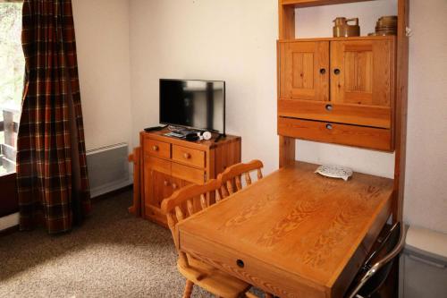Cette chambre dispose d'une table en bois et d'une commode avec une télévision. dans l'établissement Résidence Le Pouzenc - Studio calme pieds de pistes MAE-6471, aux Orres