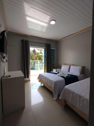 a bedroom with two beds and a television and a window at Marcone Lima - Chalés in Barreirinhas