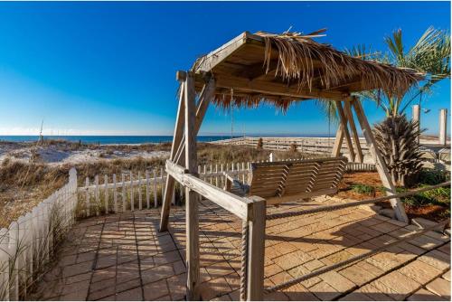 a bench under a straw umbrella on the beach at Royal Palms Unit 1205 in Gulf Shores