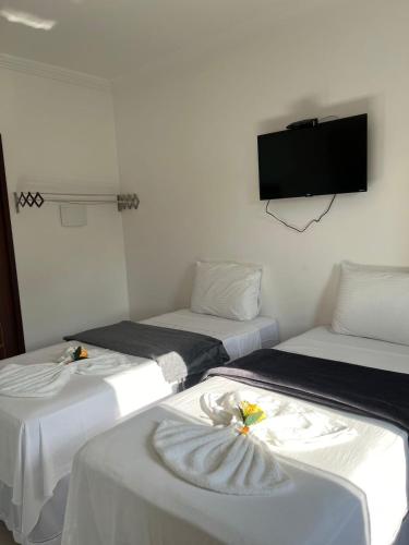 three beds in a room with a tv on the wall at Pousada La Belle in Maragogi