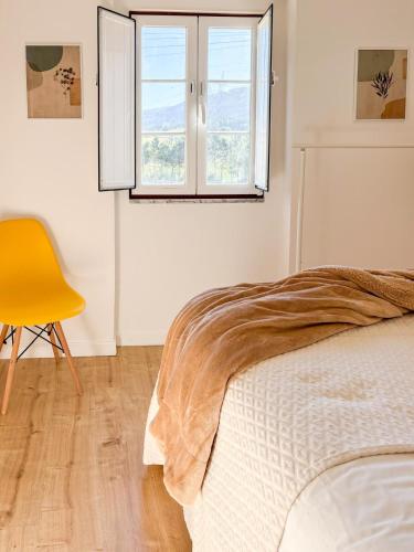 a white bedroom with a bed and a yellow chair at Casinha da Serra in Vilar