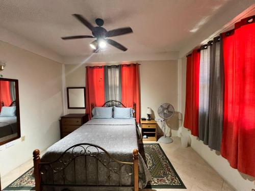 a bedroom with a bed with red curtains and a ceiling fan at The Seclusive Mansion in Roseau