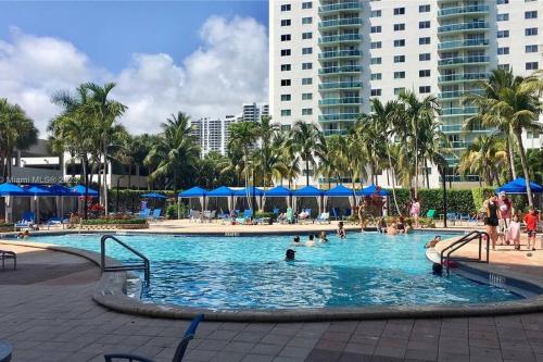 a pool with people in it with palm trees and buildings at Modern 1 BR Condo, Steps from Beach, Free Parking! in Sunny Isles Beach