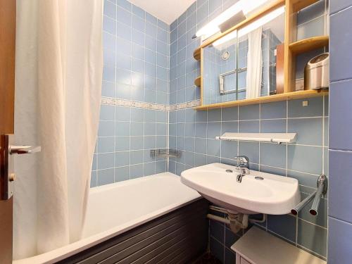 La salle de bains est pourvue de carrelage bleu, d'un lavabo et d'une baignoire. dans l'établissement Résidence Tougnette - Studio rénové lumineux · Départ et retour skis aux pieds · Balcon MAE-2724, aux Menuires