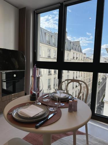 une table avec des assiettes et des verres devant une fenêtre dans l'établissement TheSuite - Parmentier - MONTHLY RENTAL ONLY, à Paris