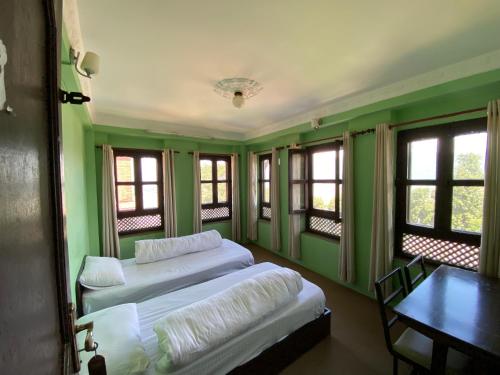 two beds in a room with green walls and windows at The Nest Guest House in Changunarayan