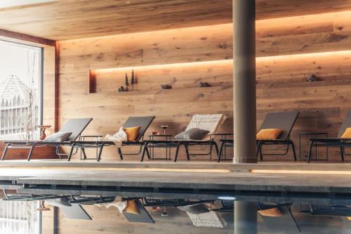 a pool with chairs and tables next to a wooden wall at Schwarzer Adler in Siusi
