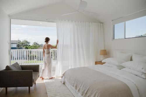 Una mujer parada en un dormitorio mirando por la ventana. en Betty at Mollymook, en Mollymook