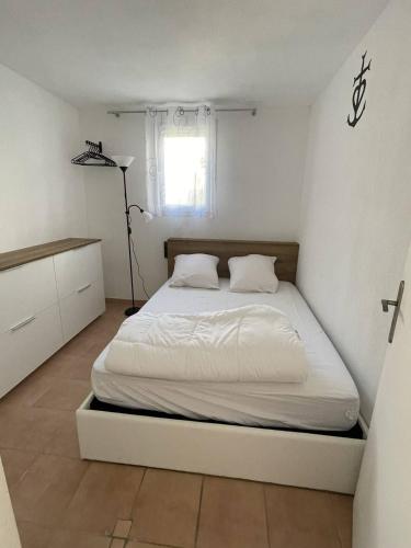 un lit dans une chambre blanche avec une fenêtre dans l'établissement Appartement T2 - place de parking - piscine collective - climatisation réversible, à Saintes-Maries-de-la-Mer