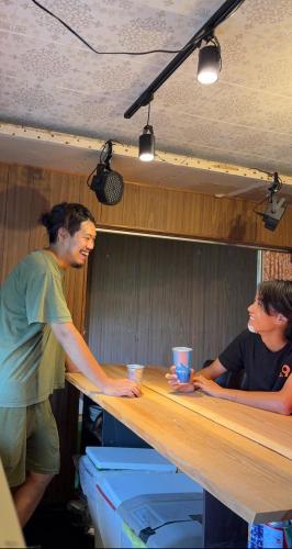 two men are standing at a wooden counter at 高野山ゲストハウス ラフテル Koyasan Guest House Laugh Tale in Hashimoto