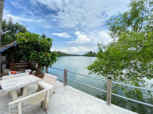 a table and bench on a deck next to the water at บ้านใบไม้โฮมสเตย์แอนด์รีสอร์ท in Surat Thani