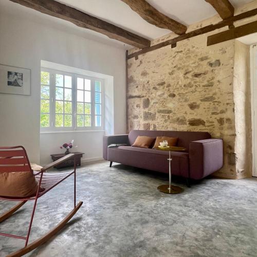 a living room with a purple couch and a stone wall at Le manoir de Jasmine in Chabrignac