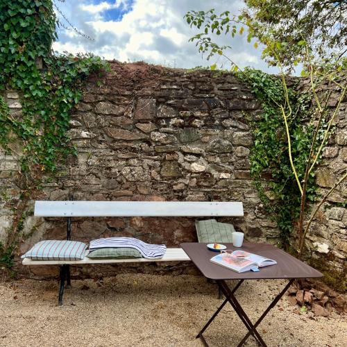 a bench and a table in front of a stone wall at Le manoir de Jasmine in Chabrignac