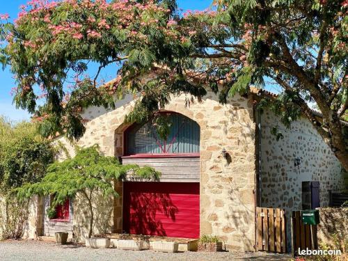 - une porte de garage rouge sur un bâtiment en pierre avec un arbre dans l'établissement Gîtes ruraux à La Gaubretière, en Vendée, à La Gaubretière