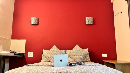 a bedroom with a red wall and a bed with a laptop on it at Arize You Homes Anjuna in Anjuna