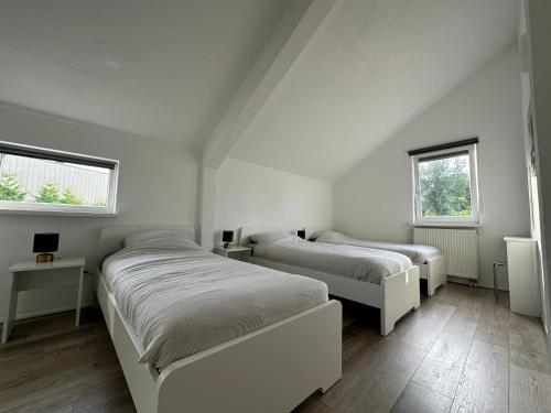 two beds in a white room with two windows at Big Family villa 12p big garden with bathtub and jacuzzi in Zeewolde