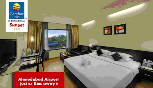 a bedroom with a large white bed and a tv at Comfort Inn Sunset in Ahmedabad