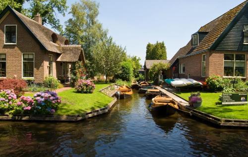 a house on a canal with boats in the water at Appartement op een boerderij met eigen tuin in Tuk