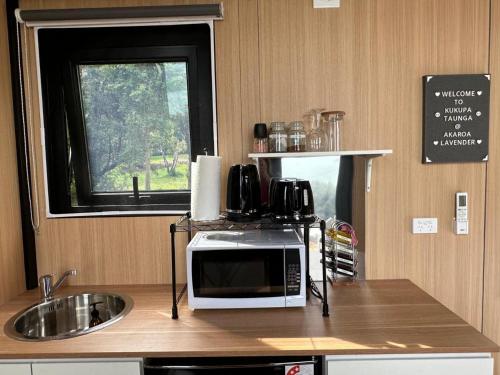 a kitchen with a microwave and a sink and a window at Kūkupa Taunga at Akaroa Lavender by Tiny Away in Akaroa