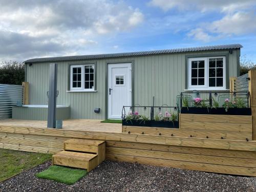 a small green house with a wooden deck at The Swallow Shepherds Hut in Perth