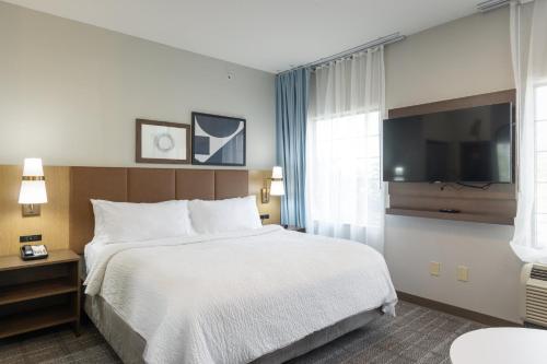 a hotel room with a bed and a flat screen tv at Staybridge Suites Rogers - Bentonville by IHG in Rogers