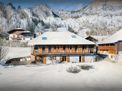 une maison dans la neige avec des montagnes en arrière-plan dans l'établissement La Ferme des Artistes - OVO Network, à Mieussy