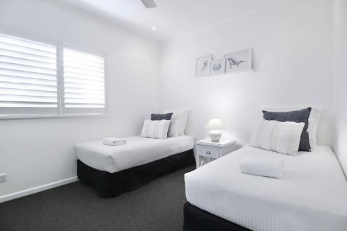 two beds in a room with white walls and a window at Bright and Airy 2 Bedroom Apartment in Noosaville