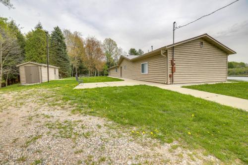 a house with a grassy yard next to a building at Waterfront Evart Getaway with Fire Pit on 82 Acres! in Evart