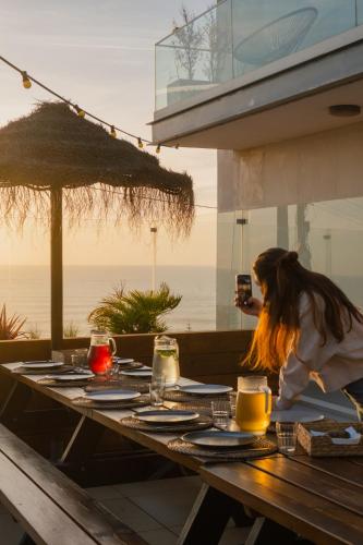 a woman taking a picture of a picnic table with the ocean at The Salty Surf & Yoga in Ericeira