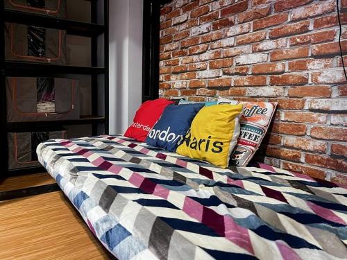 a bed with colorful pillows and a brick wall at Stylish Studio Dave Apt Depok with Pool, WiFi, Netflix by 2ndHome in Pondoktjina Tiga
