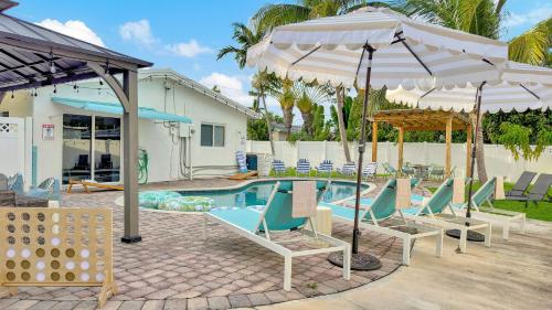 a pool with chairs and umbrellas in front of a house at Sunset Oasis with Movie Theatre, Heated Pool & Game Room in Pompano Beach
