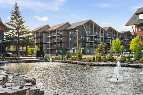 an exterior view of a building with a pond and fountain at NEW Spacious MTN View Condo, PRIME location with Hot Tub, Free National Park Pass, Huge Patio, BBQ, Sleeps 7 in Canmore