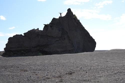 a large rock with a person standing on top of it at South Coast Panorama in Hvolsvöllur