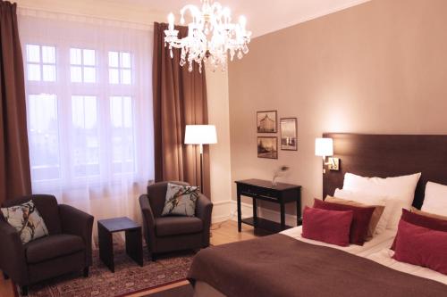 a bedroom with a bed and two chairs and a chandelier at Home Hotel Drott in Karlstad