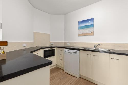 a kitchen with white cabinets and a black counter top at Charlesworth Bay Beach Resort in Coffs Harbour