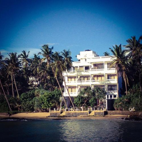 duży biały budynek na plaży z palmami w obiekcie Mirissa Seastar w mieście Mirissa