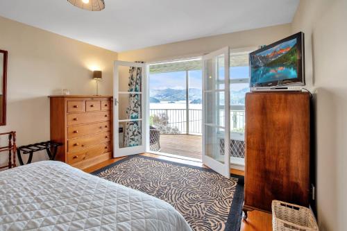 a bedroom with a bed and a television and a balcony at Bayview Beauty - Charteris Bay Holiday Home in Diamond Harbour